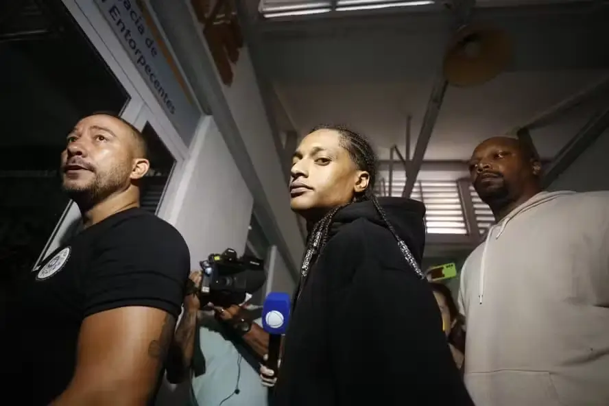 O rapper Mauro Davi Nepomuceno, mais conhecido como Oruam se entrega à polícia na noite desta terça-feira (22), após ter sua prisão decretada pela Justiça. O artista chegou à Cidade da Polícia, no Jacarezinho, no banco traseiro de uma SUV preta, acompanhado da noiva, Fernanda Valença, da mãe, Márcia Nepomuceno, e de seus advogados. Após prestar depoimento, Oruam foi encaminhado à Divisão de Capturas da Polícia Interestadual (Polinter), onde ficará até a audiência de custódia marcada para esta quarta-feira (23). Depois, será transferido para o presídio de Benfica, na Zona Norte do Rio. O cantor teve a prisão preventiva decretada após se envolver em uma confusão com policiais da Delegacia de Repressão a Entorpecentes (DRE), que cercaram sua residência no bairro do Joá, Zona Oeste da cidade. Segundo a Polícia Civil, o episódio ocorreu durante uma operação para apreender um adolescente acusado de atuar como segurança de um chefe do Comando Vermelho. Oruam foi indiciado por desacato, resistência qualificada, lesão corporal, ameaça e dano. A Justiça alegou ainda que o rapper utilizava sua casa para abrigar criminosos foragidos e que suas postagens nas redes sociais “incitam desobediência civil e resistência contra o Estado Democrático de Direito”. Em sua defesa, o cantor afirmou ter sido vítima de abuso de autoridade e que só reagiu após ser ameaçado com armas de fogo pelos policiais. Ele também disse que pertences seus e de sua noiva foram danificados durante a ação policial. Oruam, filho de Marcinho VP — um dos chefes históricos do Comando Vermelho —, já se envolveu em outras polêmicas e passagens pela polícia. Em fevereiro, foi preso por abrigar um foragido da Justiça em sua casa e, recentemente, provocou os agentes em vídeos gravados no Complexo da Penha, desafiando a prisão.